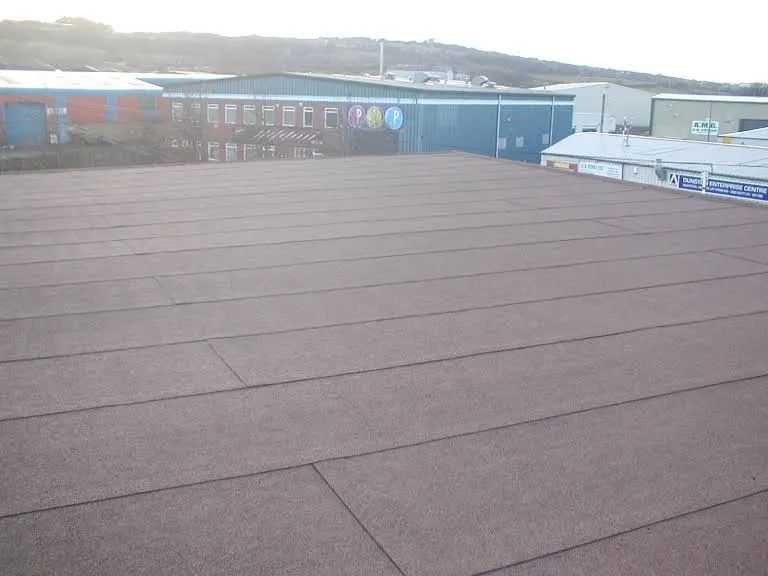 Brown flat roof with horizontal lines, buildings in the background.
