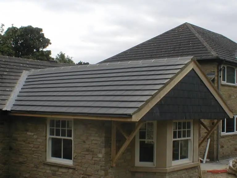 Gray tiled roof over a bay window, beige brick house, cloudy sky.