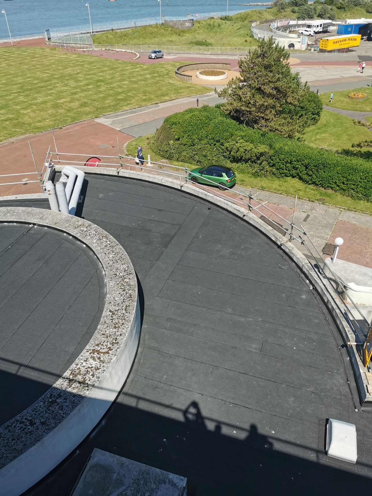 Overhead view of a curved road with a green car, near a grassy area and a bus stop.