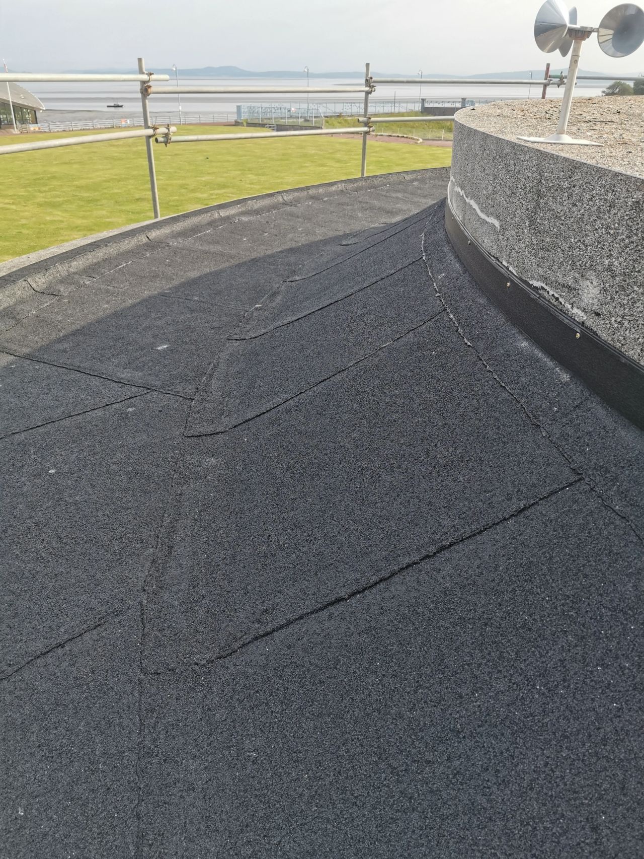 Black rubber roof with markings, curved edge, and green lawn in background.