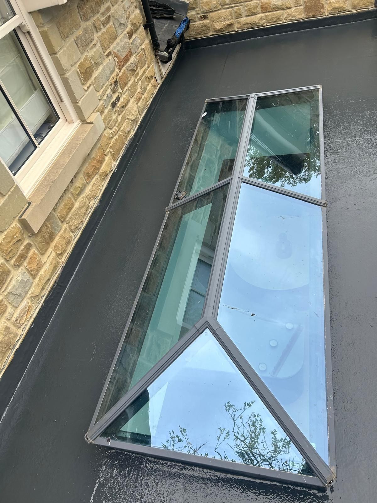 Geometric glass skylight on a flat black roof next to a stone wall.