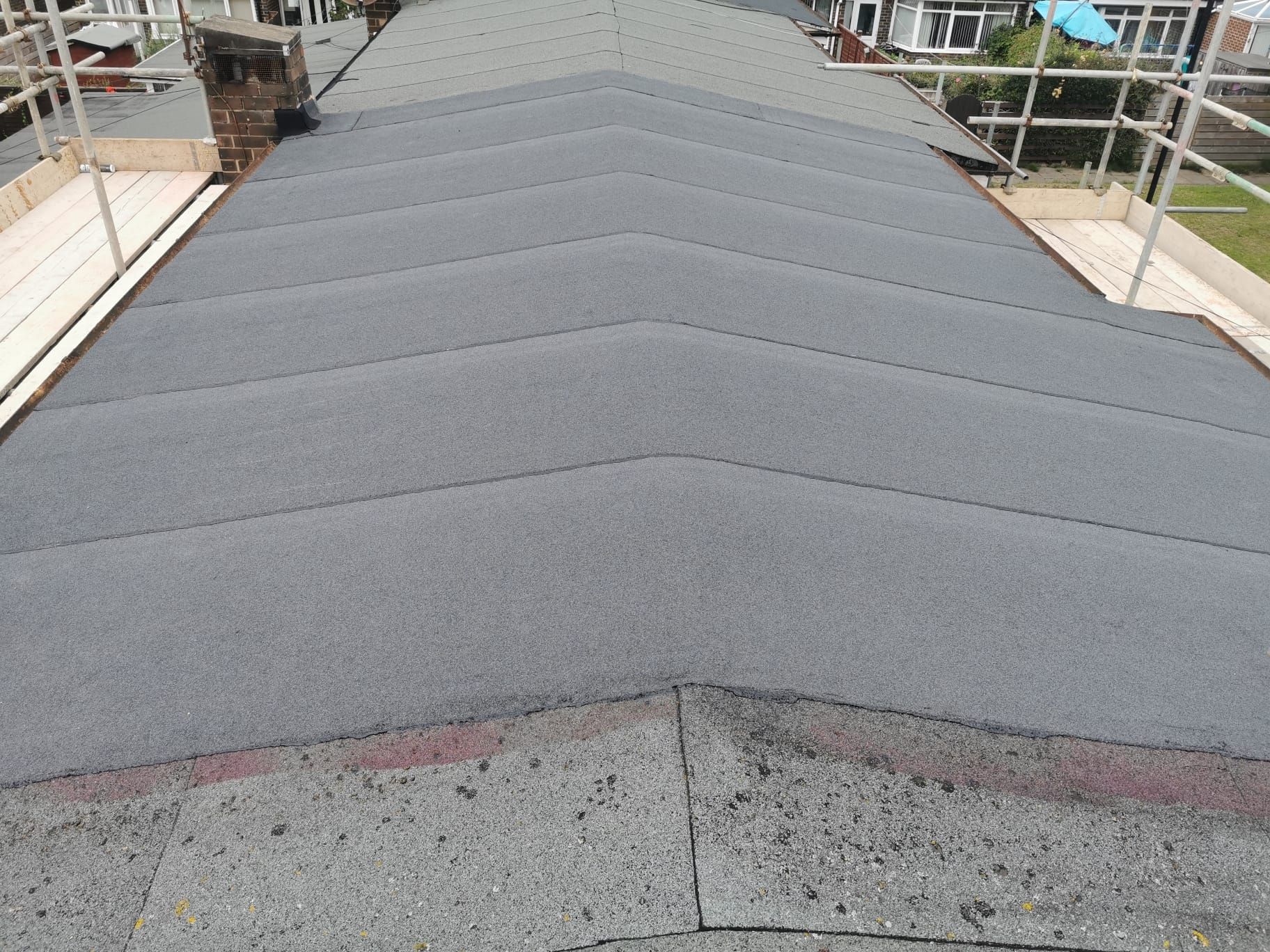 A gray, angled asphalt shingle roof with a chimney and safety railings.