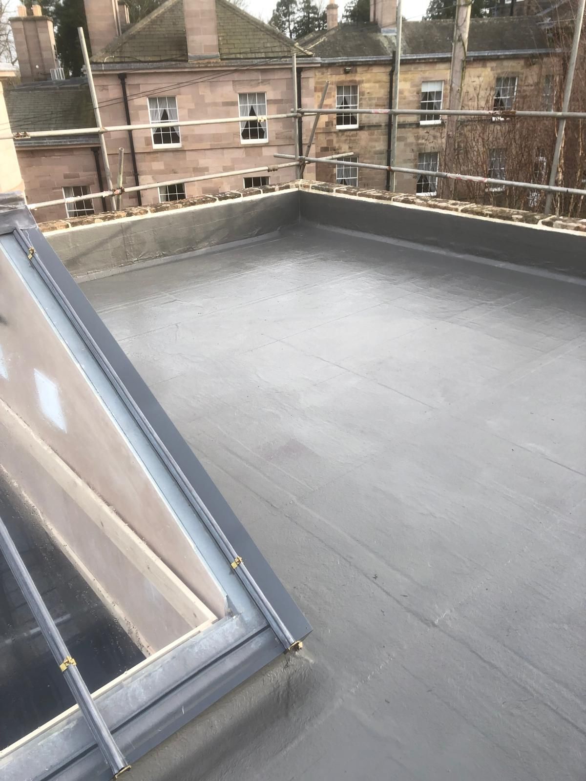 Flat, gray roof with a skylight. Buildings and scaffolding in the background.