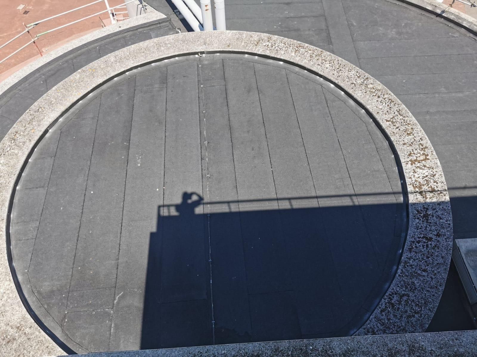 Overhead view of a circular rooftop with a person's shadow. The roof is bordered by a stone wall.