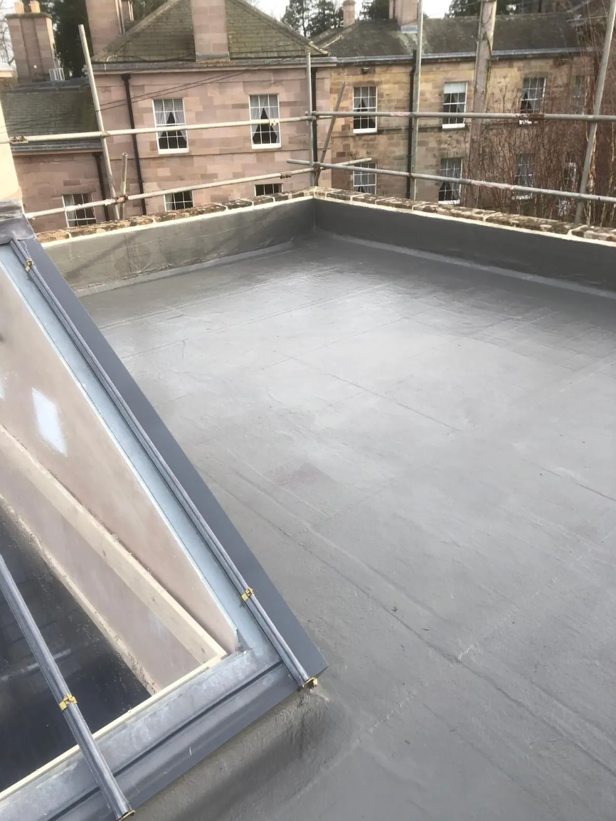 Flat gray roof with glass skylight, surrounded by buildings with scaffolding.