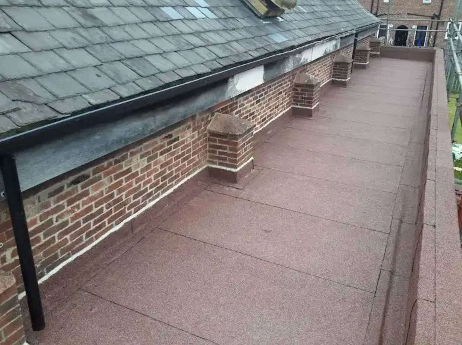 Flat roof with brick wall and dark slate roof, brown granules on the surface.