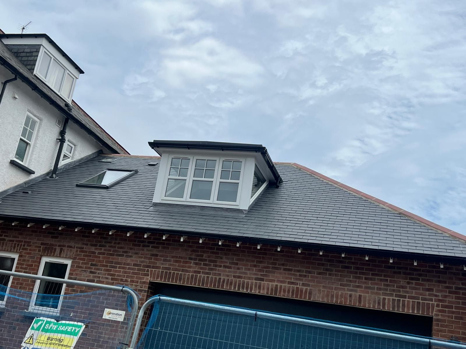 Brick building with a dark gray shingled roof, dormer window, and sky background.