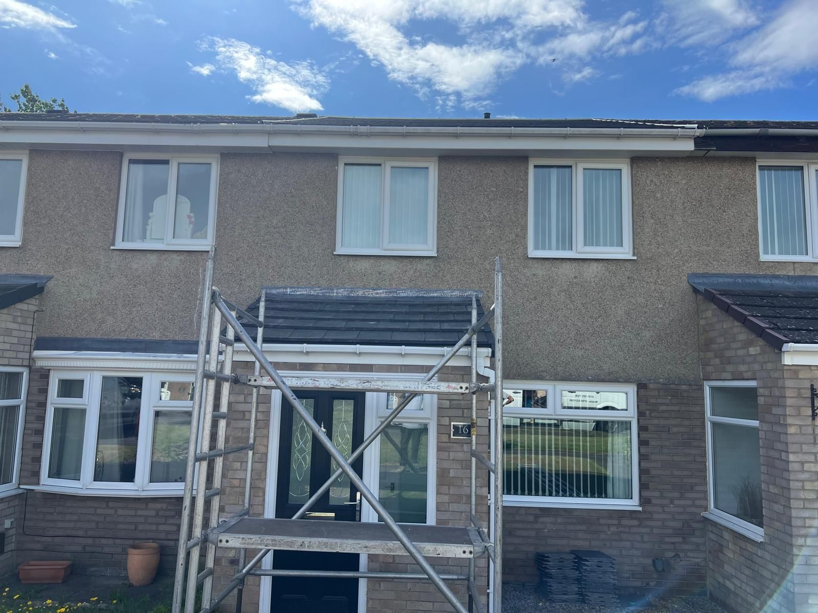 Row houses with scaffolding, light brown stucco, white windows, blue sky.