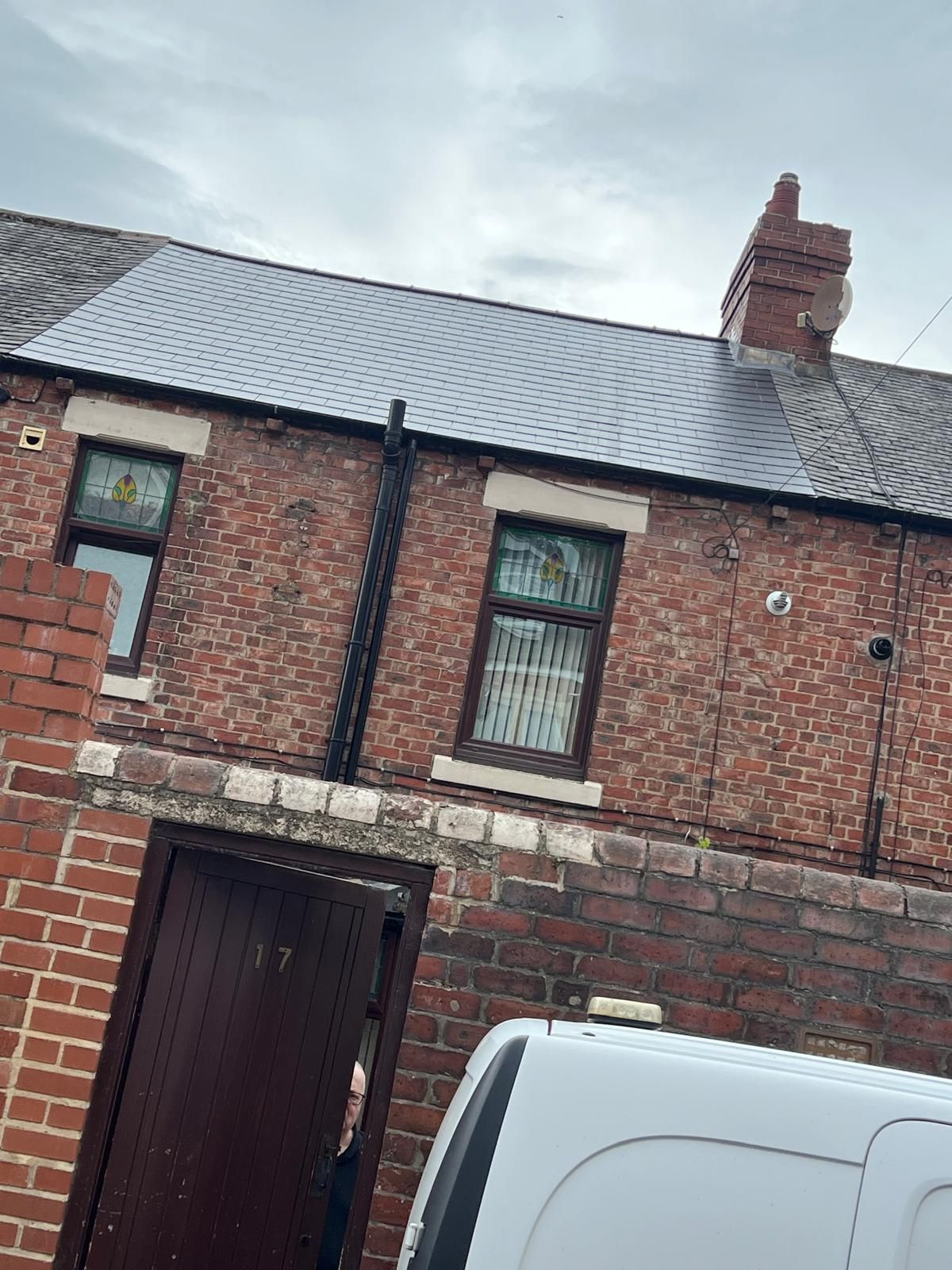 Brick row house with two windows, chimney, and dark brown door; white van partially visible in front.
