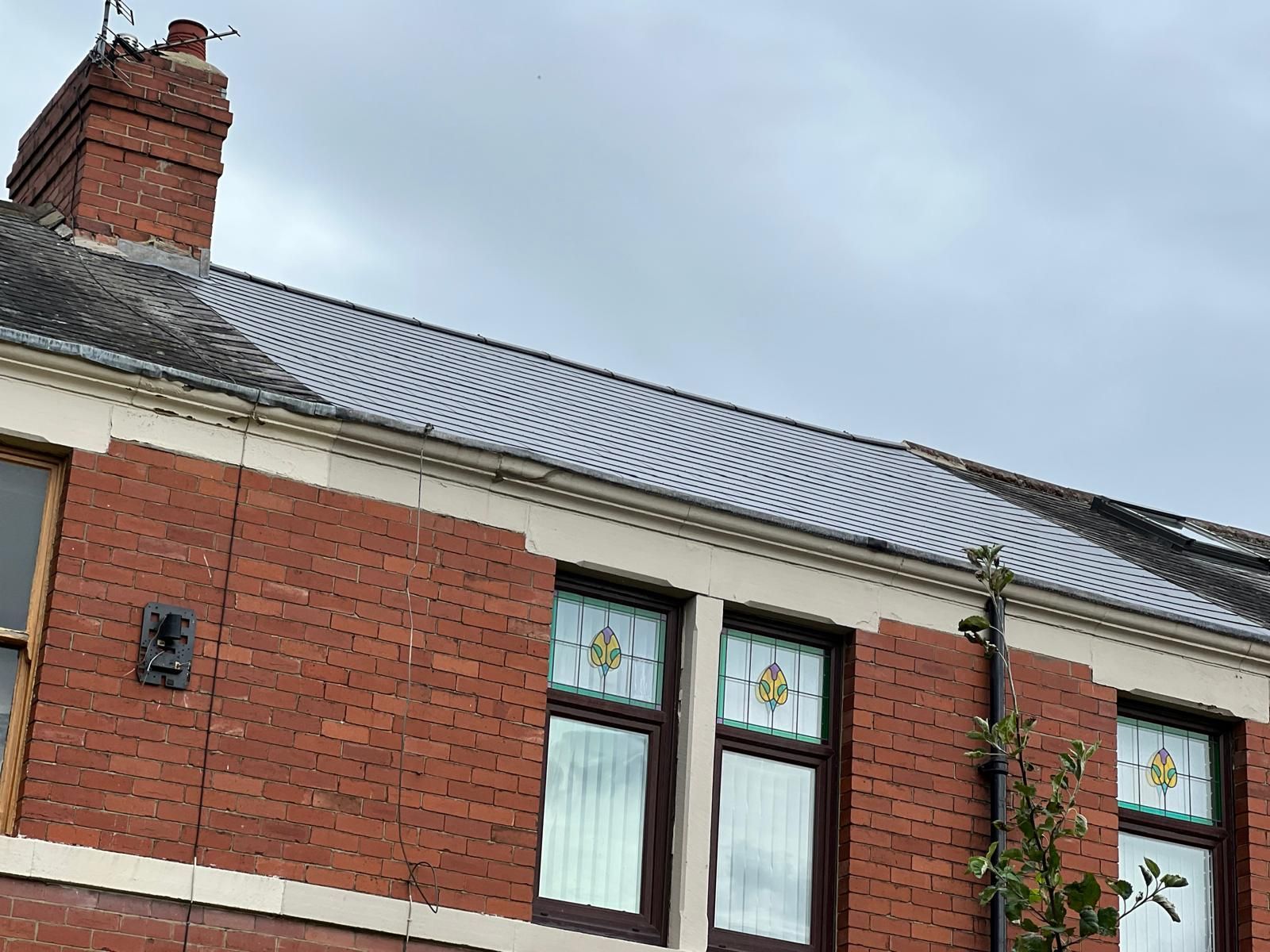 Red brick house with gray tiled roof and stained glass windows under a cloudy sky.
