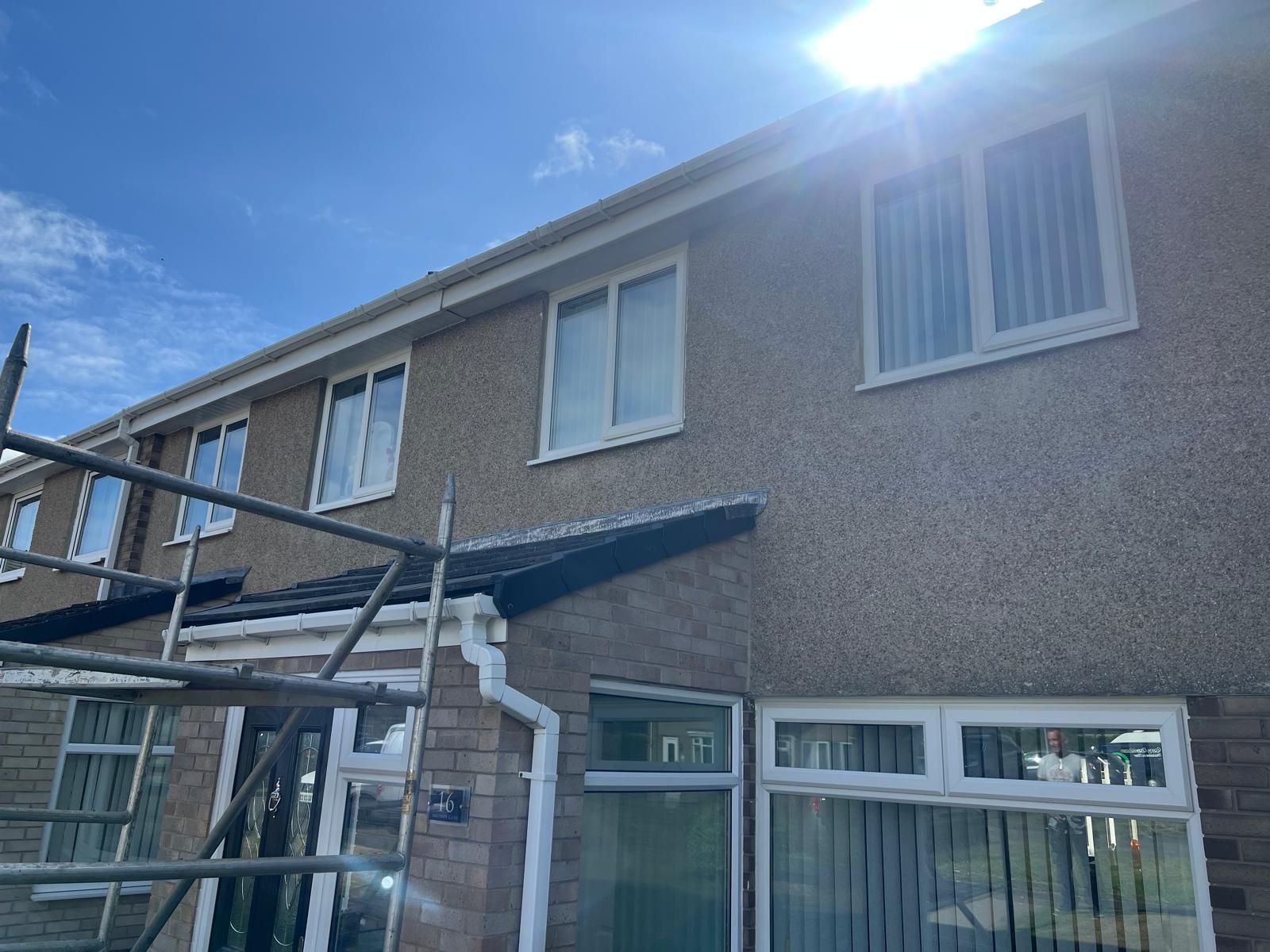 Exterior of a two-story house with scaffolding set up. Light brown stucco, white windows, blue sky.