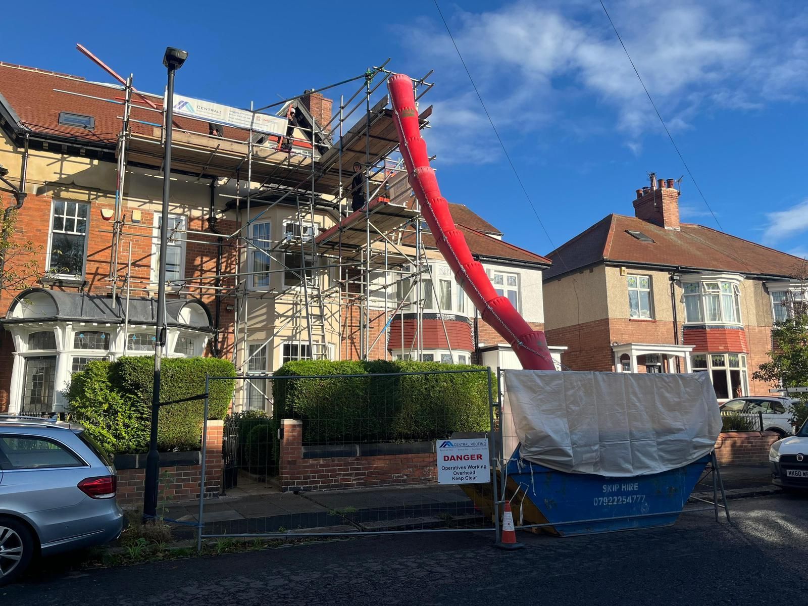 Scaffolding on a house with a red chute leading to a covered dumpster; construction work.
