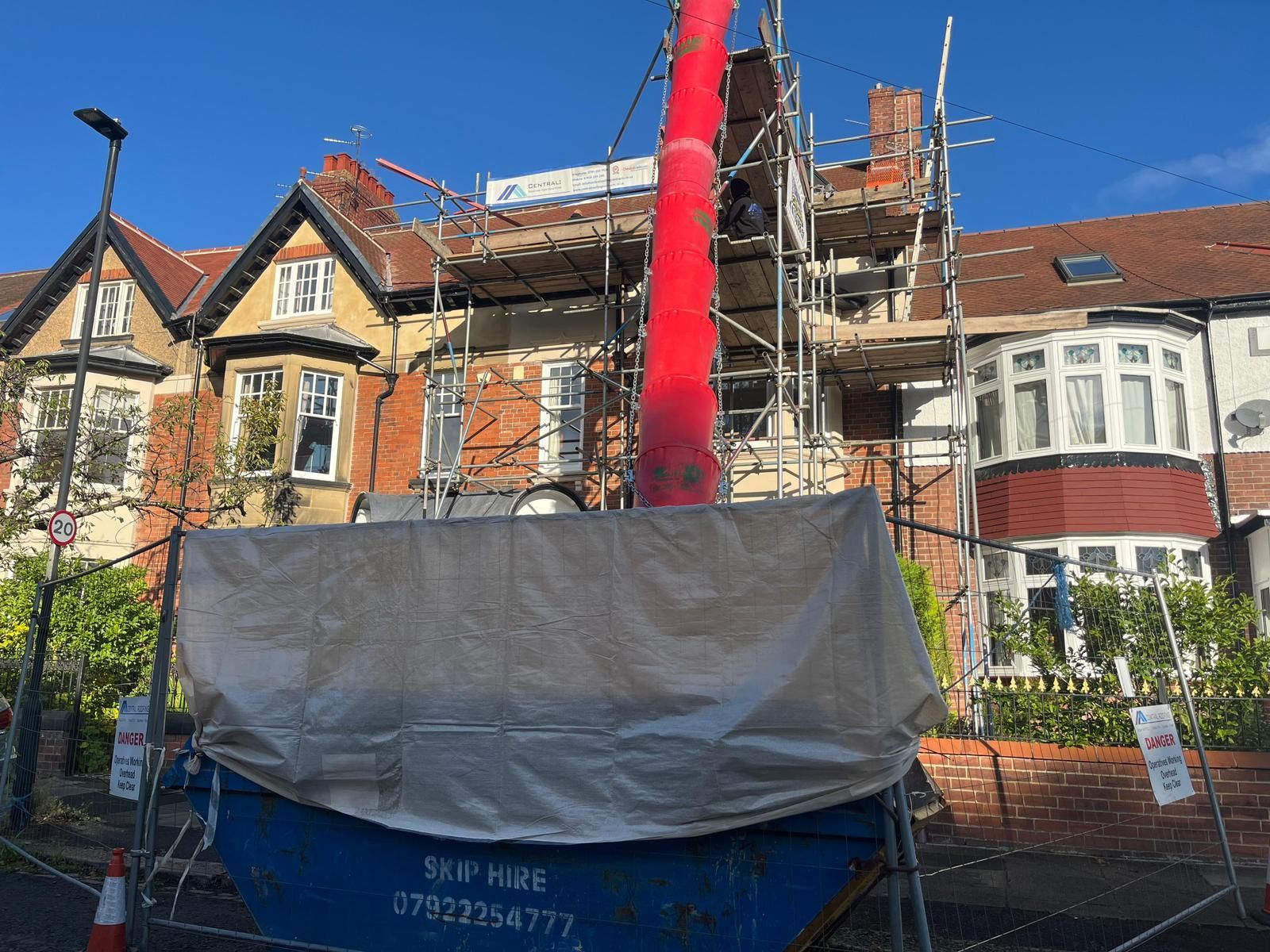 A residential house under renovation with scaffolding, a debris chute, and a skip.