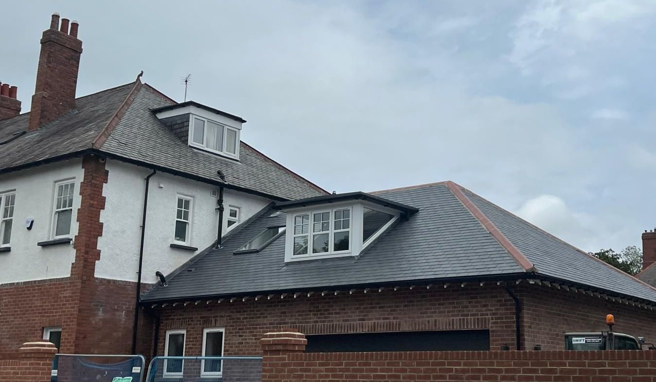 Building with red brick and white exterior walls, dark roof with dormers, and overcast sky.