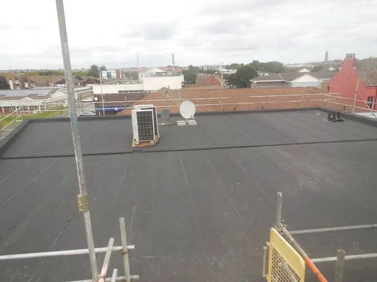 Black flat roof with equipment, overlooking a neighborhood on an overcast day.