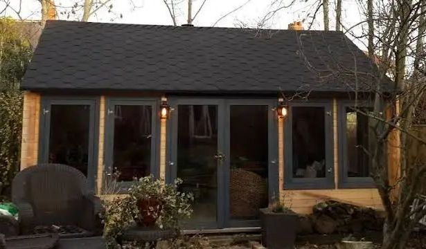 A garden shed with glass doors and windows, gray frames, and a dark shingled roof.