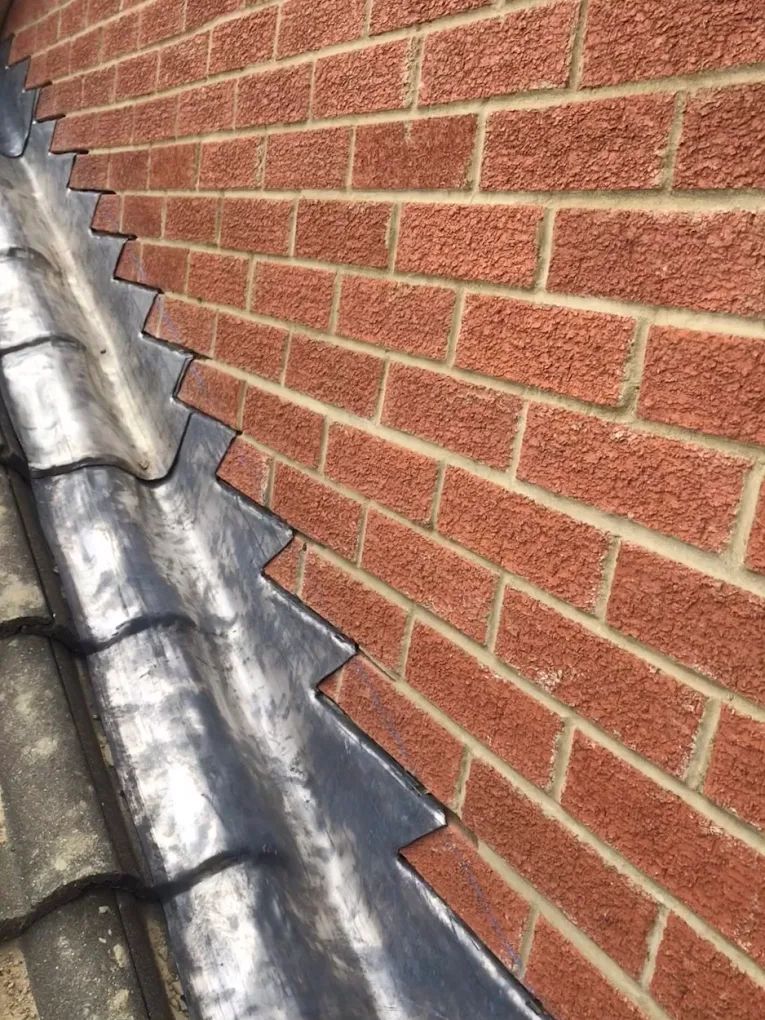 Close-up of brick wall with zigzagged lead flashing covering the roof tiles.