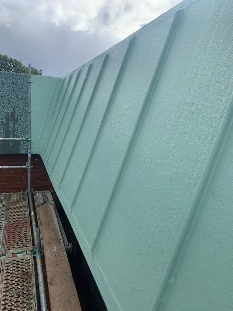 Green metal roof with vertical panels, next to scaffolding and brick.