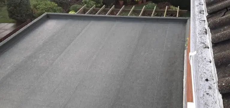 Flat, gray roof with wooden beams, and a gutter with old tiles.