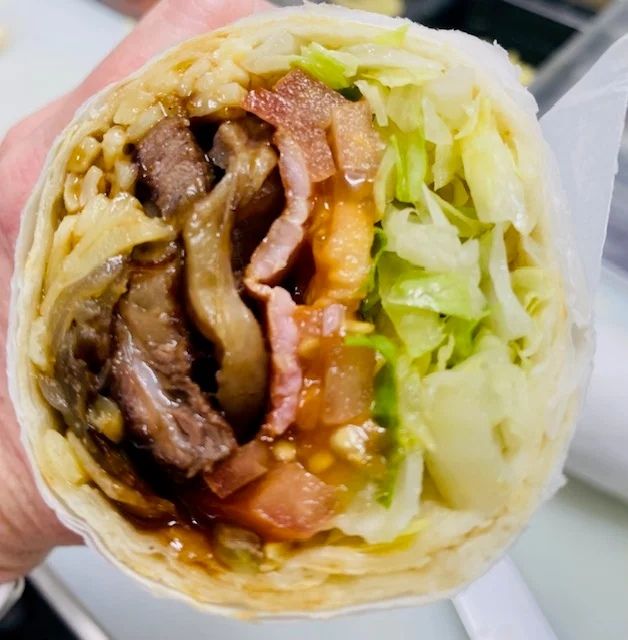 A Person is Holding a Burrito With Meat and Lettuce — Cedar Park Fish & Chips In Taranganba, QLD