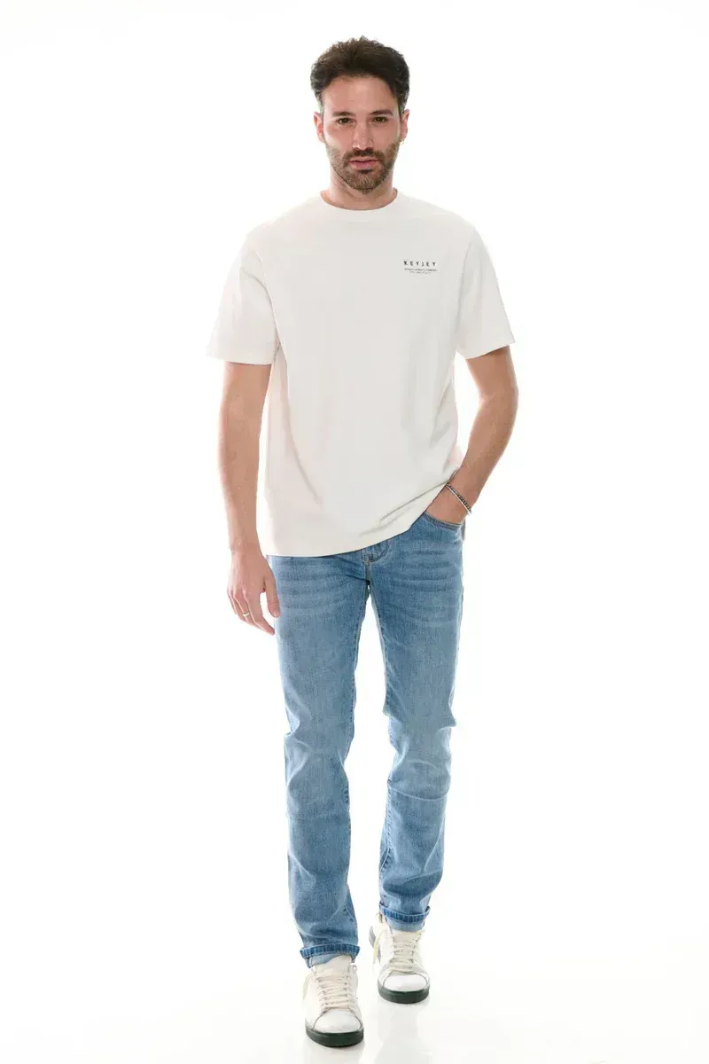 Un uomo che indossa una maglietta bianca e jeans blu è in piedi con le mani in tasca.