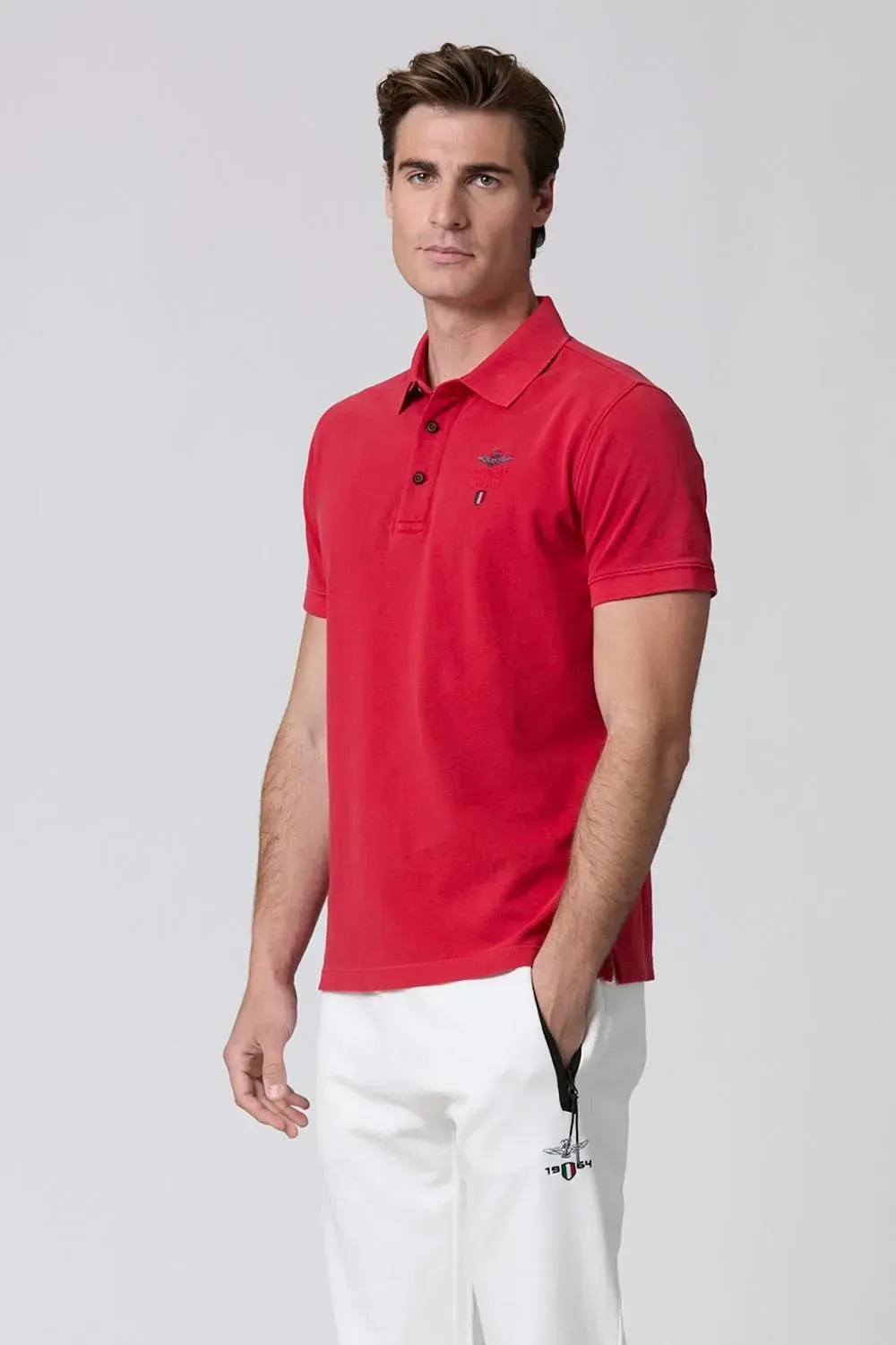 Un uomo indossa una polo rossa e pantaloncini bianchi.