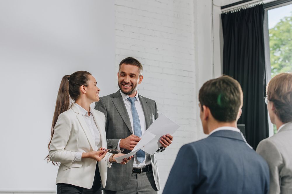 Hombres de negocios vestidos de traje sonriendo, dando una presentación en una oficina moderna.