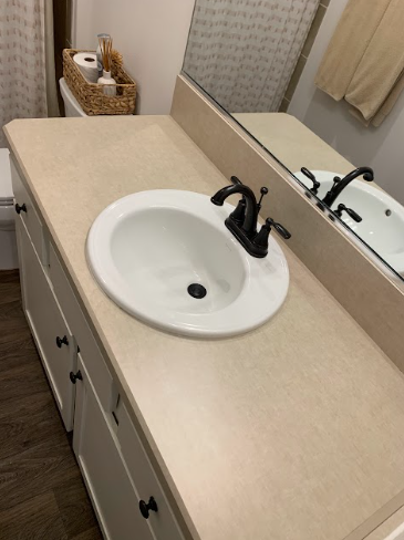 Bathroom vanity with beige countertop, white sink, black faucet, and large wall mirror.