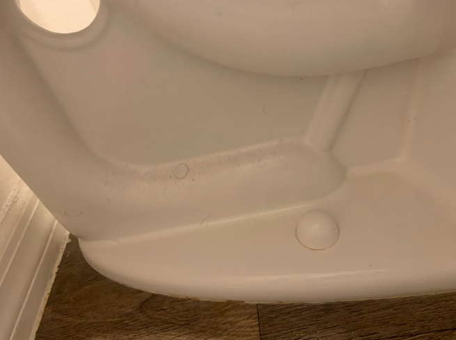 Close-up of a white plastic object with a circular button on a wood floor.