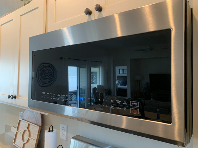 Black stainless steel microwave mounted above a kitchen counter with white cabinets and a tiled backsplash