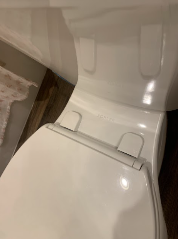 Close-up of a white toilet seat and lid in a bathroom, viewed from above.