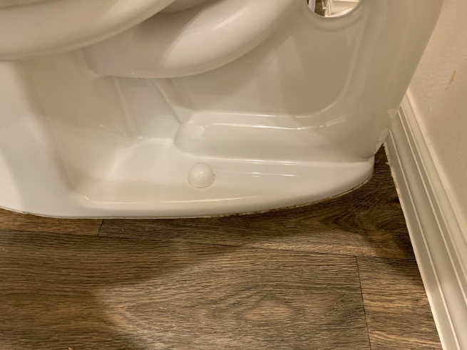 Toilet base with visible gap near wall over wood floor in bathroom