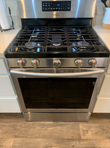 Stainless steel gas range with four burners, digital control panel, and oven in a modern kitchen