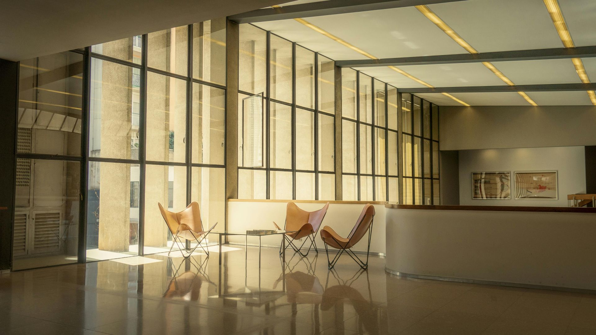 Modern office lobby with glass walls, wooden chairs, and warm sunlight reflecting on the polished floor