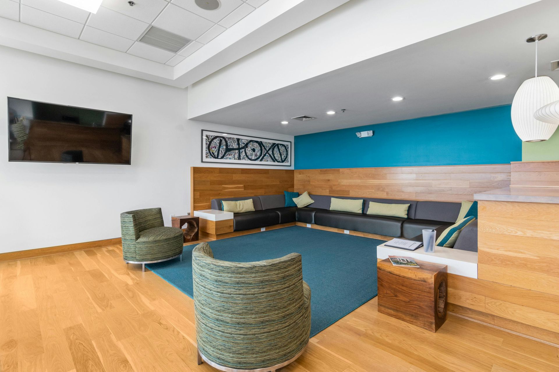 Modern lounge with blue and wood accents, woven chairs, sectional sofa, and wall-mounted TV.