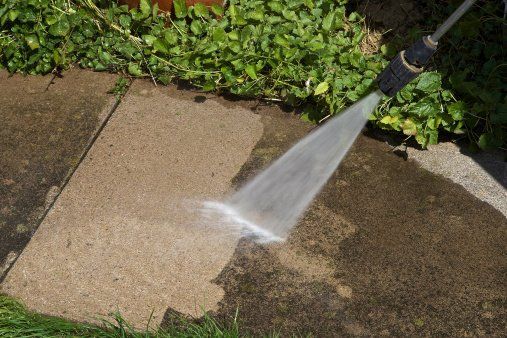 A person is using a high pressure washer to clean a sidewalk.