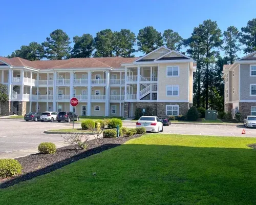 Exterior view of light yellow condo building with parking lot and trees.