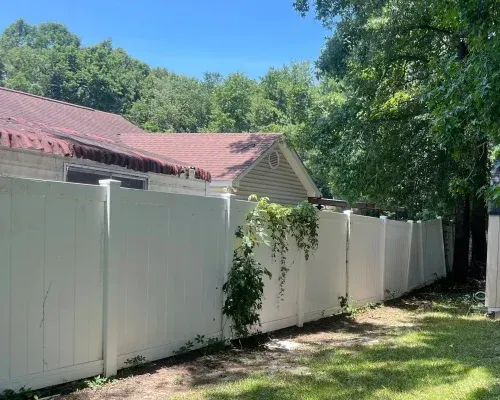 White vinyl fence in a grassy yard, partially obscuring a building with a red roof.