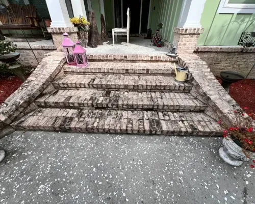 Brick steps leading up to a house entrance; pink lanterns, a white chair, and plants are present.