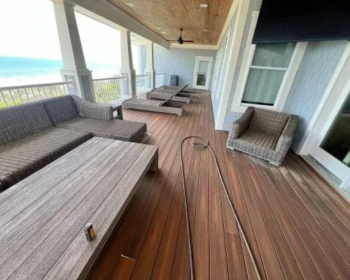 A wooden deck with ocean views features a sectional sofa, lounge chairs, and a coffee table.