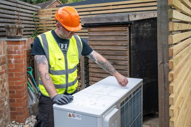 A man wearing a hard hat and safety vest is working on an air conditioner.