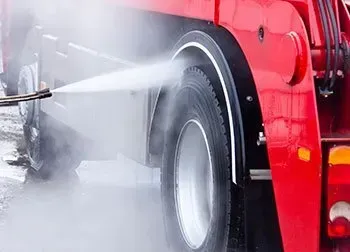 A person power washes a house siding with a yellow nozzle, removing dirt outdoors.