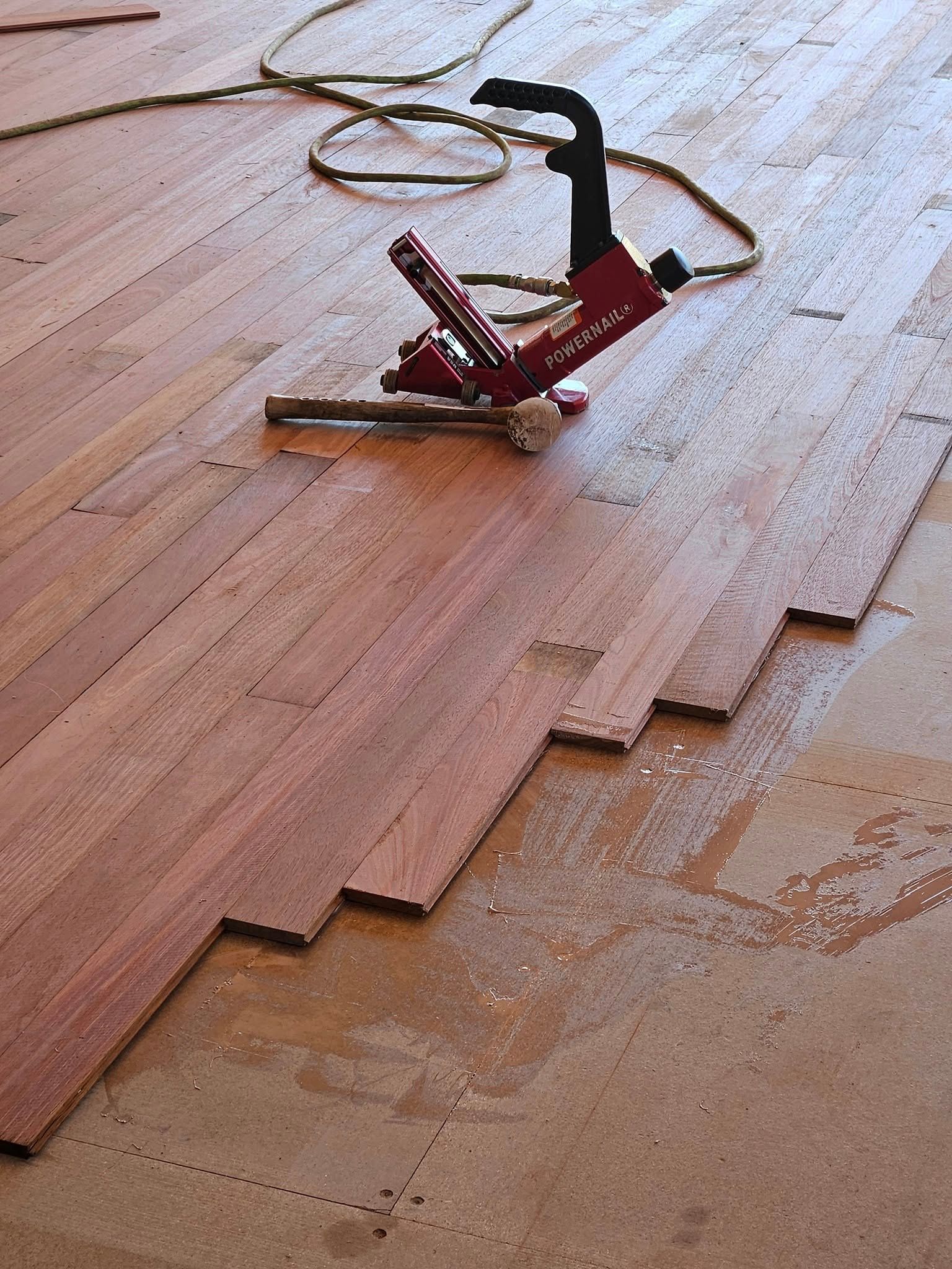 A red stapler is sitting on a wooden floor.