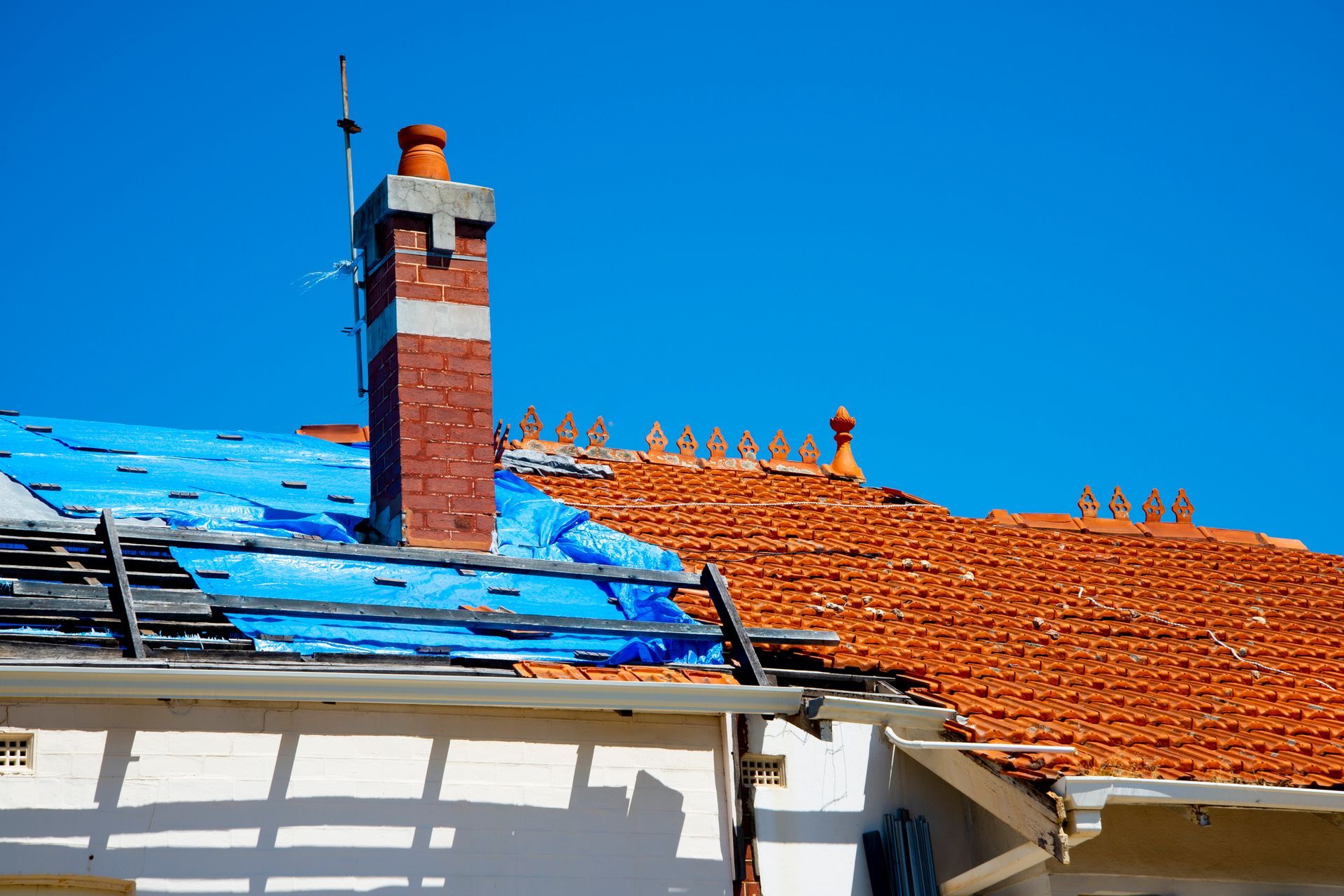 Roofing restoration with partially completed roof, blue tarp, and chimney.