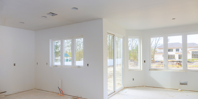 Two rooms in an unfinished state, white walls, large windows, bare floors, and ceiling fixtures.