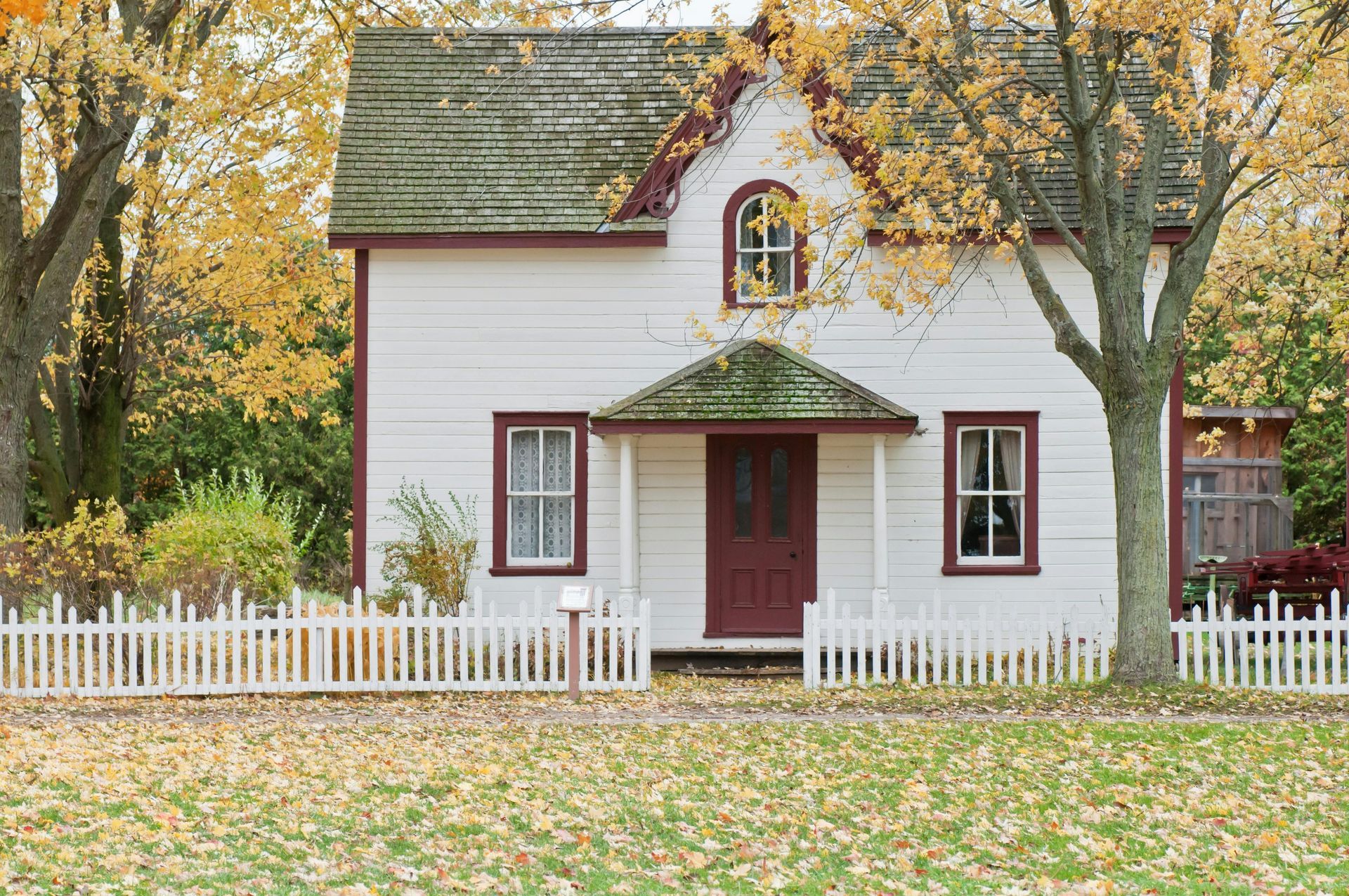 White house with red trim, picket fence, and autumn trees.