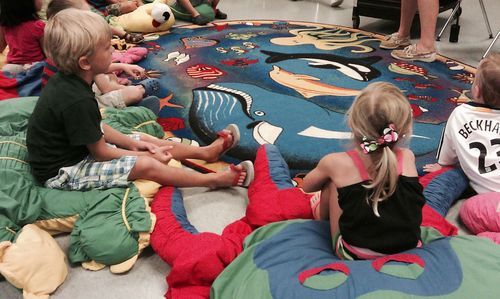 Children sitting on mats, focused on a colorful rug depicting aquatic life; indoors.
