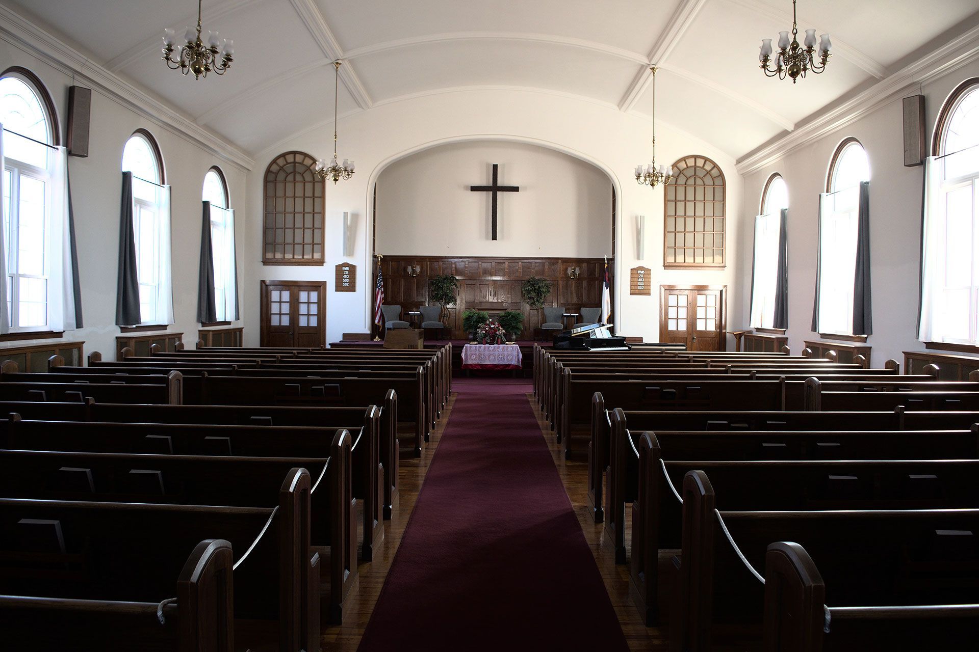 Interior of a church with rows of wooden pews, a red carpet, and a cross on the altar.