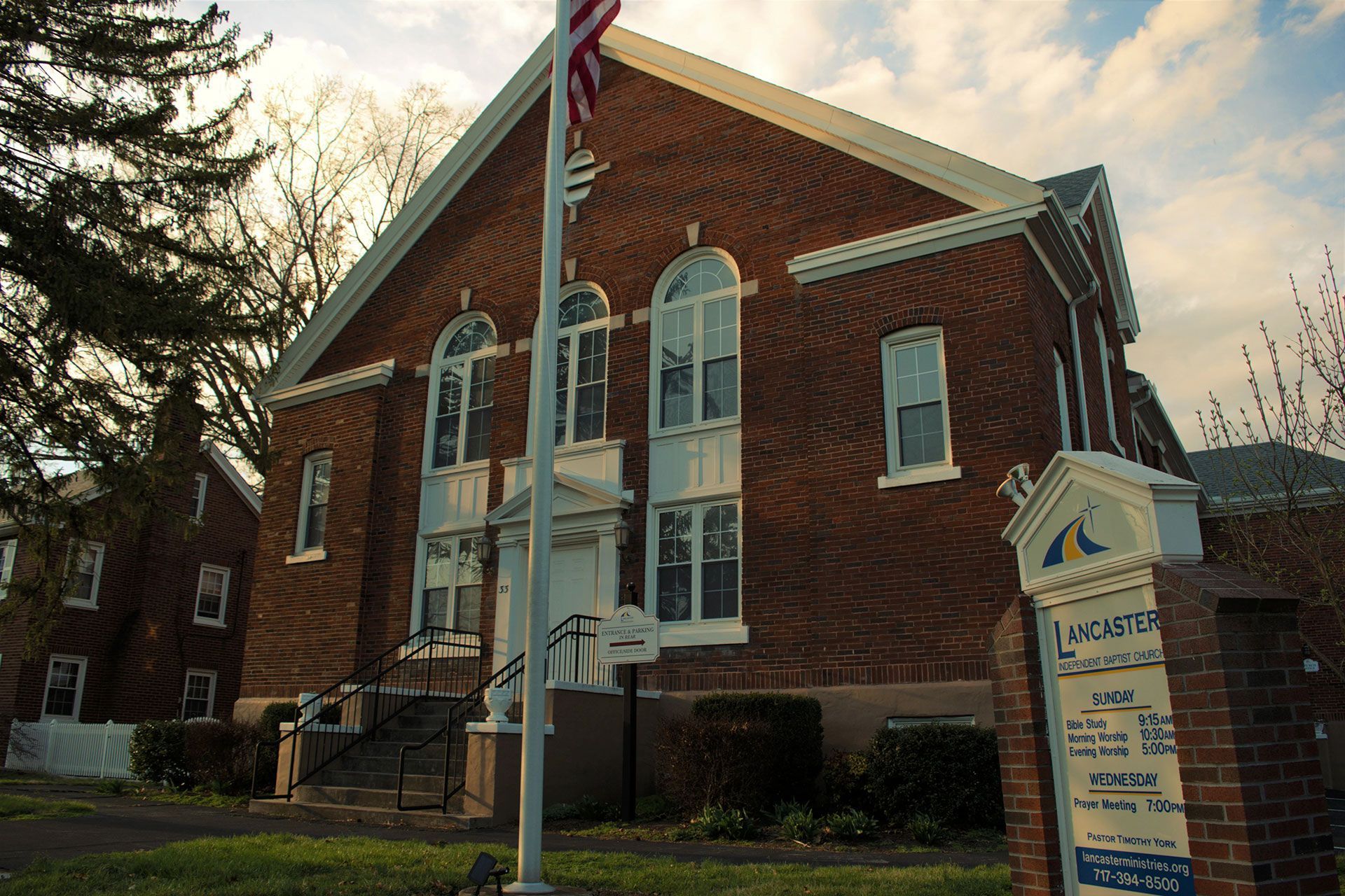 Brick building with white trim, flag pole, and sign reading 