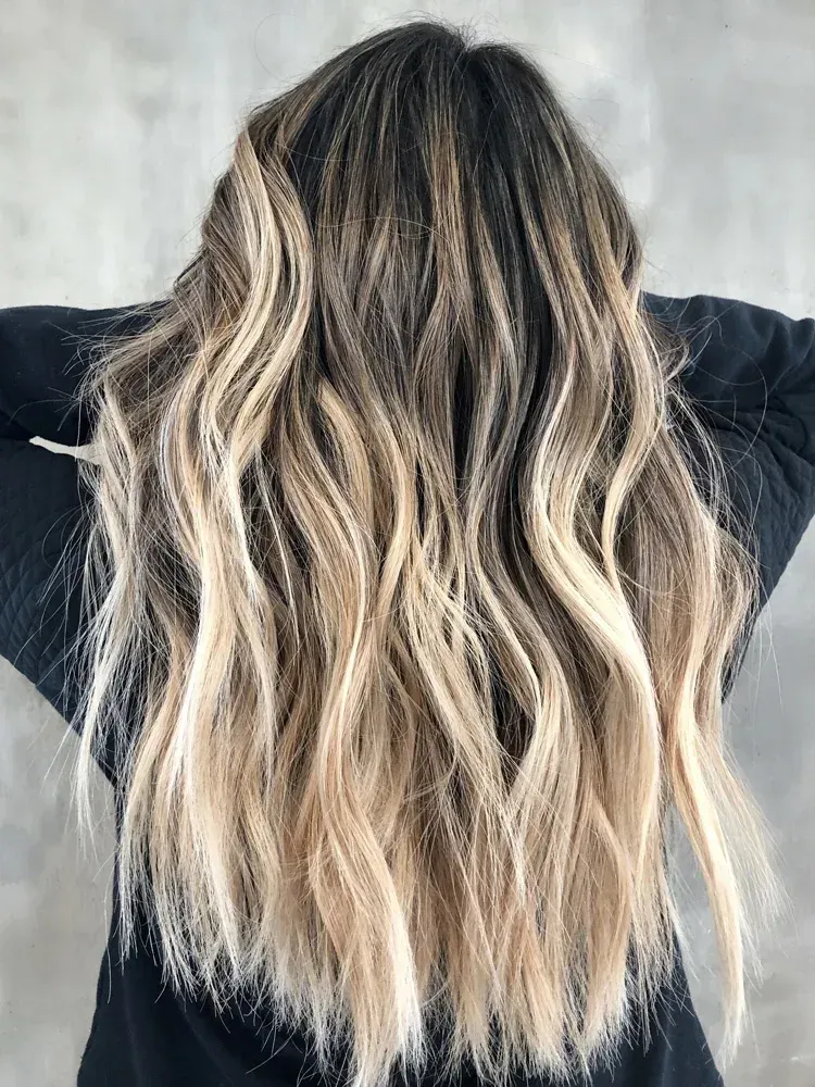 Mujer con cabello largo y ondulado que presenta una raíz oscura que se desvanece a rubia, sostenida frente a ella.